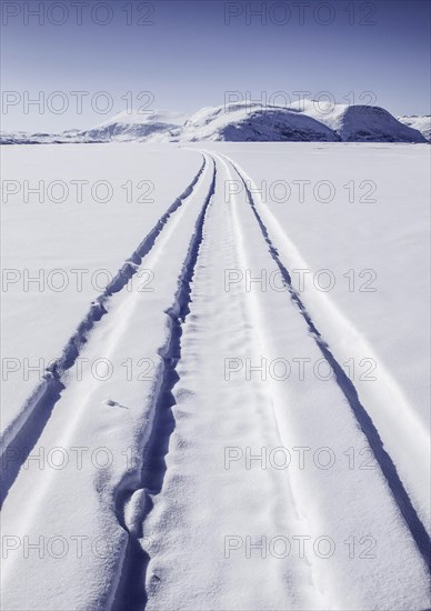 Driving tracks head off across a frozen fjord towards distant mountains