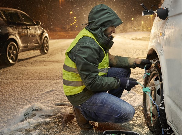 Man with safety vest applying snow chains on snow-covered road