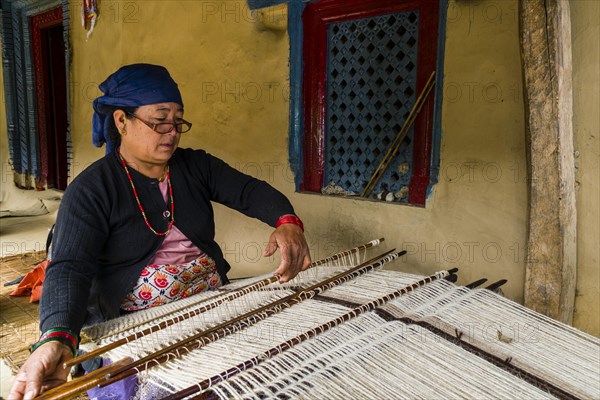 Native woman weaving blanket using sheep's wool in front of house