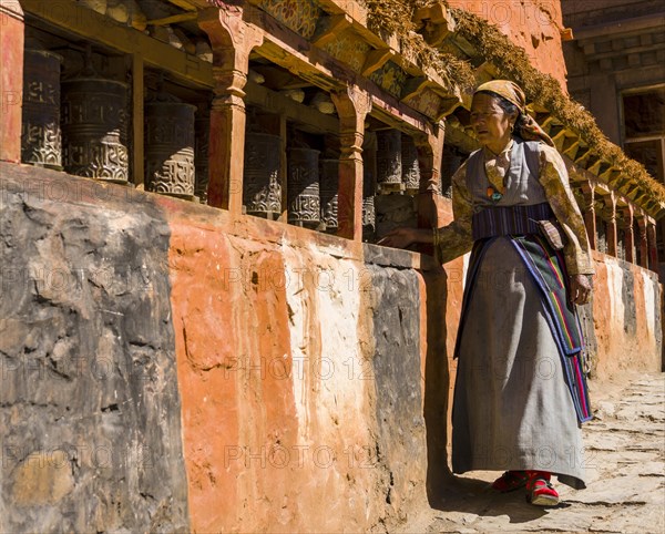 Native woman walking along Mani Wall and spinning prayer wheels