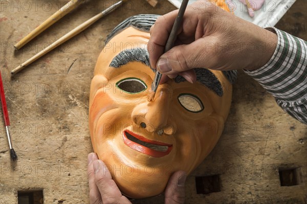 Painting the face of a wooden mask with a paintbrush