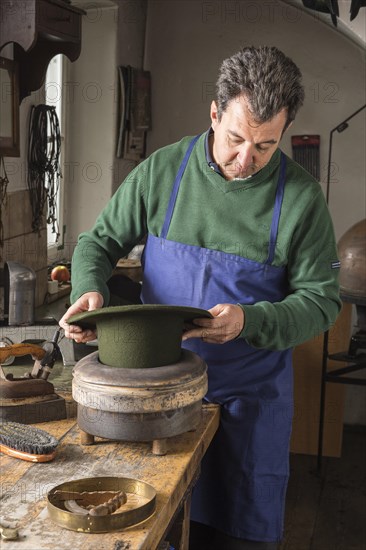 Hatter pushing dry wool felt hat into edge mold