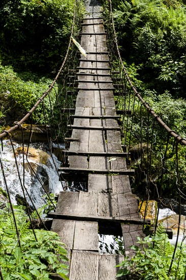 Old wooden suspension bridge across small river in Upper Modi Khola valley