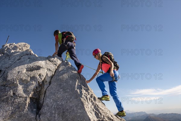 Mountain guide guiding a young woman on a short rope through a rock face