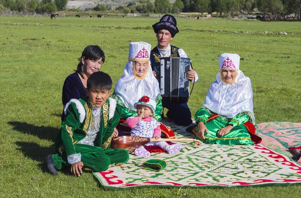 Kazakh family in traditional clothes listening to the music of an accordion player