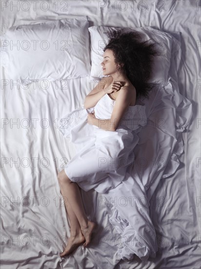 Overhead photo of a young woman sleeping alone in bed covered with a bedsheet in a bedroom