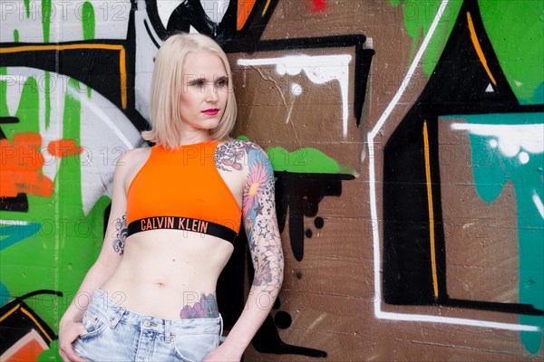 Young blond tattoo model posing at graffiti wall