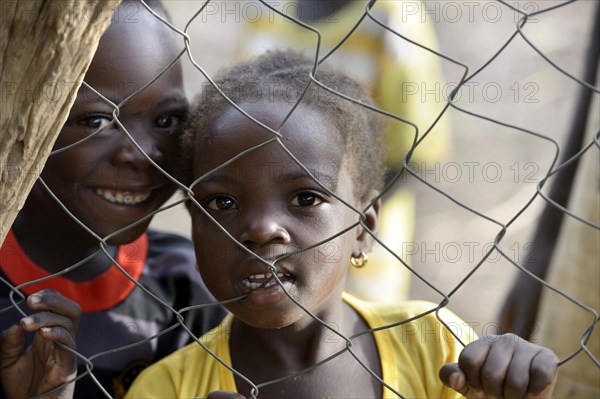 Two children looking through wire mesh fence