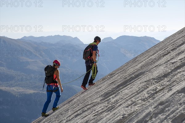 Mountain guide guiding a young woman on a short rope through a rock face