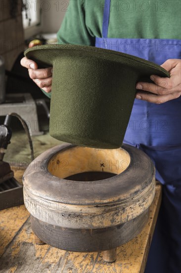 Hands holding dry wool felt hat over an edge mold