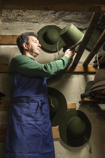 Hatter placing wool felt hat with shaping cord to dry on wooden boards in drying room