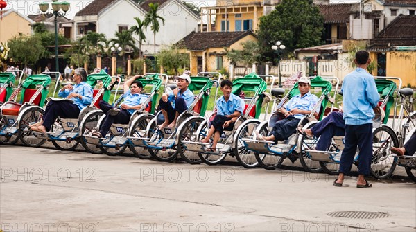 Rickshaw riders sit in their bicycle rickshaws at the roadside