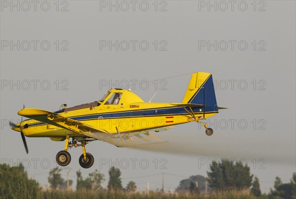 Crop duster plane flying low while spraying an anti mosquito substance onto the rice fields