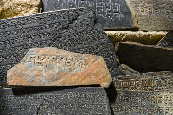 Mani stones with the engraved tibetan mantra Om Mani Padme Hum are piled up to a wall