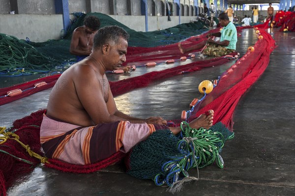 Local men repairing fishing nets in hall at harbour