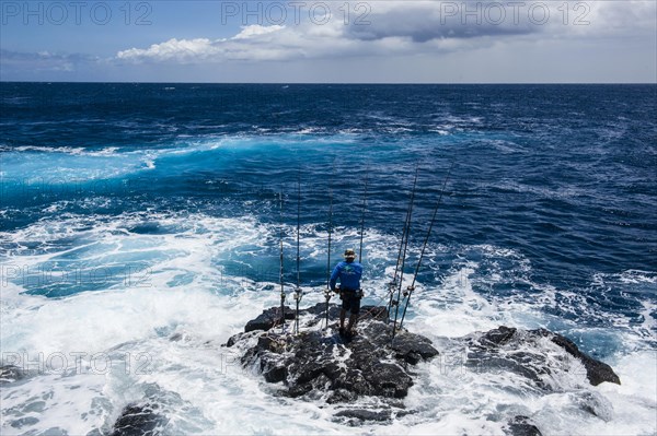 Fisherman standing on a rock in The Sea with his angling rods