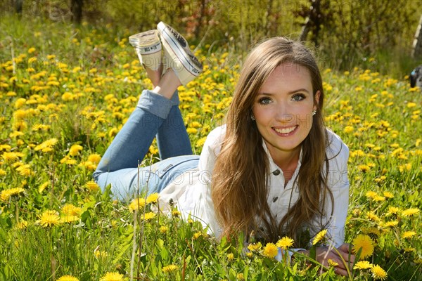 Young woman lying in a meadow of dandelion