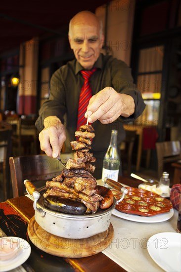 Older man serving traditional brasero or grilled meat