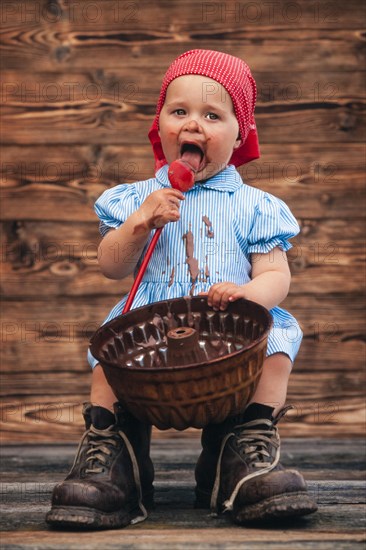 Three-year-old girl eating chocolate cake mixture from cake tin