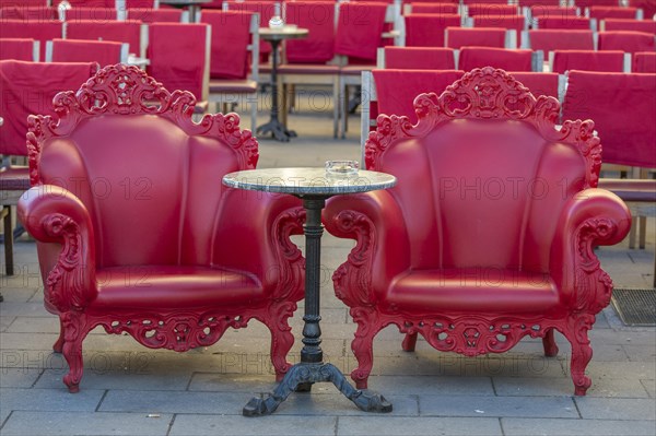 Two stately red armchair next to each other at bistro table with ashtray