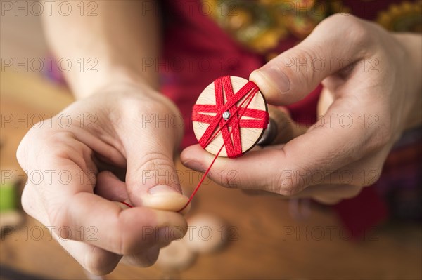 Button maker in third step of Posamentenknopfe production holding wooden blank with vise and carefully wrapping red yarn
