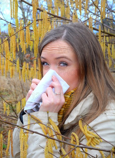 Woman with pollen allergy among flowering hazel (Corylus)