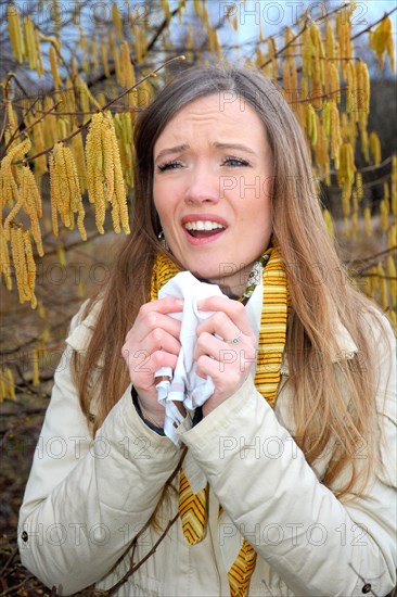 Woman with pollen allergy among flowering hazel (Corylus)