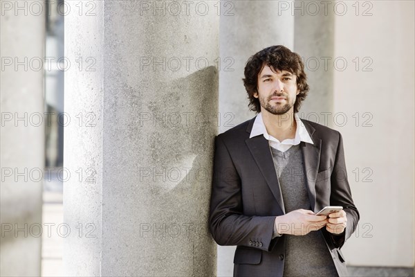 Young man leans on column with smartphone in hand