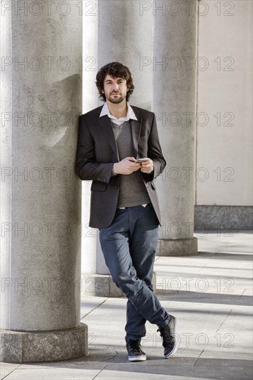 Young man leans on column with smartphone in hand