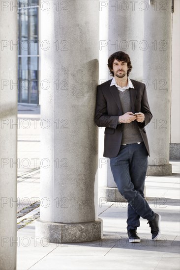 Young man leans on column with smartphone in hand