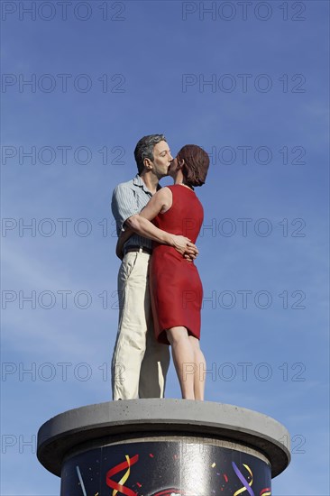 Kissing couple on an advertising pillar in front of a blue sky