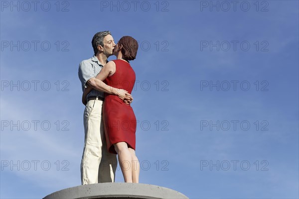 Kissing couple on an advertising pillar in front of a blue sky