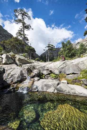 Young man sitting next to a pool with small waterfall in the mountains