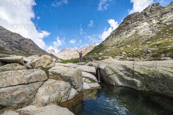 Young man standing next to a small waterfall with pool in the mountains