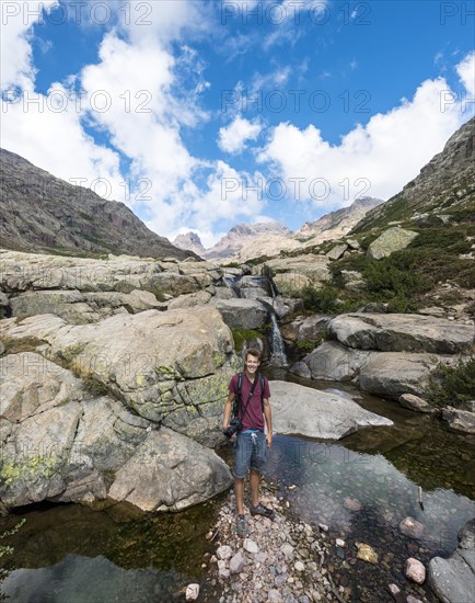 Young man standing at a pool with a small waterfall in the mountains