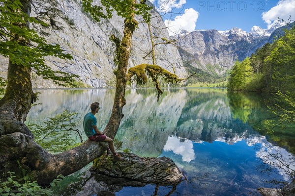 Young man sitting on tree above water