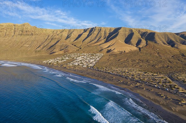 View on beach Playa Famara with bungalows and mountain range Risco de Famara