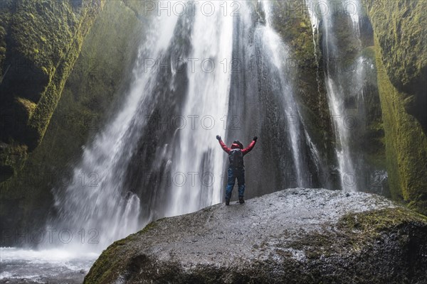 Hiker on rocks in front of Gljufrabui Waterfall in Hamragardar