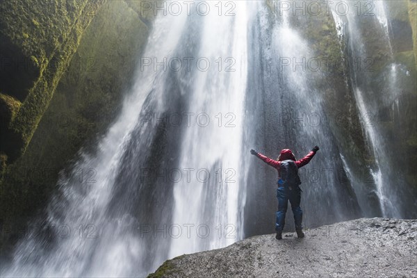 Hiker on rocks in front of Gljufrabui Waterfall in Hamragardar