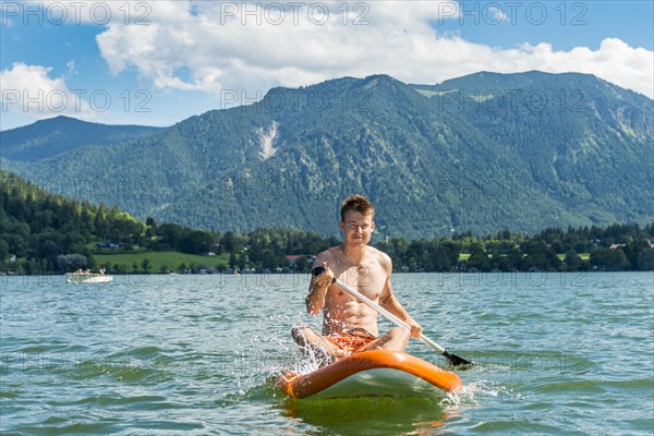 Young man sitting on a paddle board on Lake Schliersee
