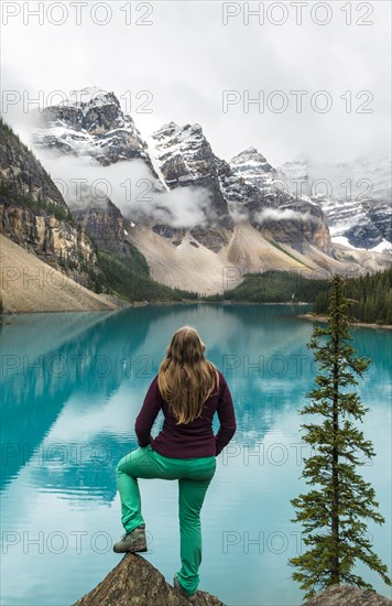 Young woman standing in front of a lake looking into mountain scenery