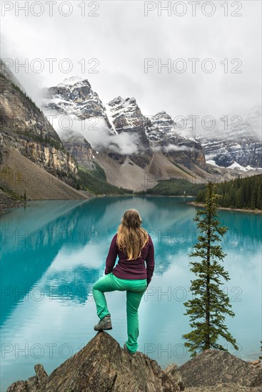 Young woman standing in front of a lake looking into mountain scenery