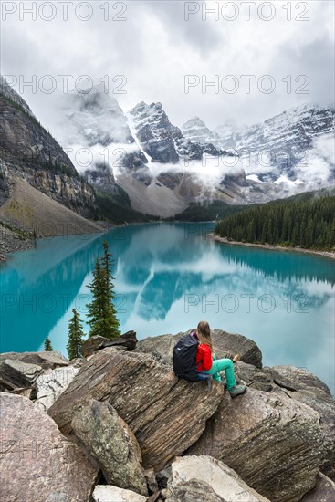 Young woman sitting in front of a lake looking into mountain landscape