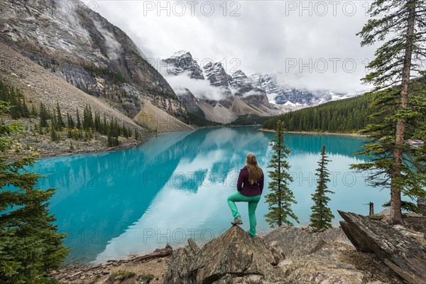 Young woman standing in front of a lake looking into mountain scenery