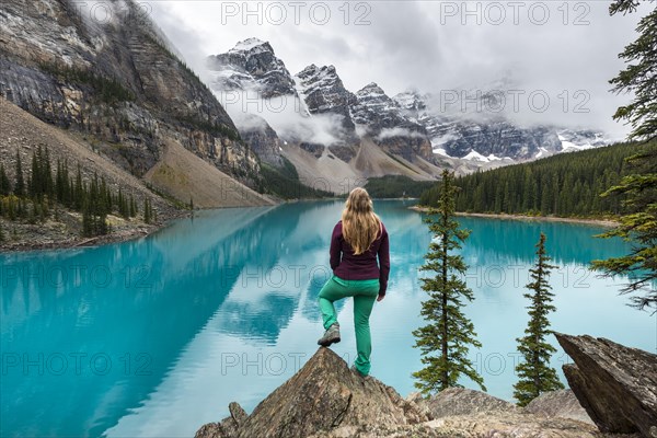 Young woman standing in front of a lake looking into mountain scenery