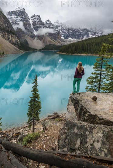 Young woman standing in front of a lake looking into mountain scenery