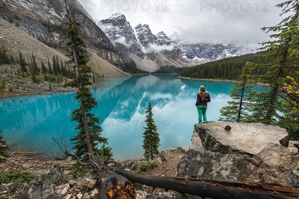 Young woman standing in front of a lake looking into mountain scenery