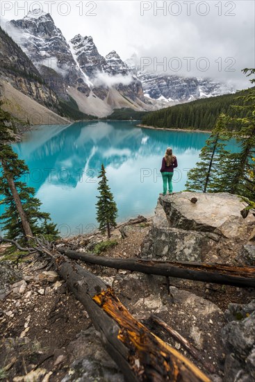 Young woman standing in front of a lake looking into mountain scenery