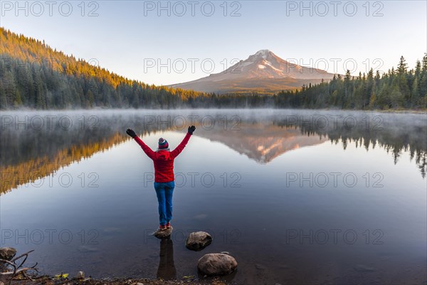 Young woman looking at view of volcano Mt. Hood with reflection in lake Trillium Lake