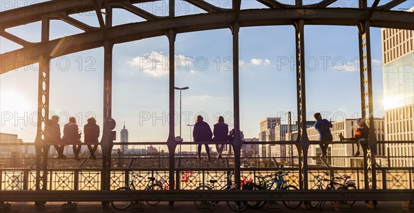Young people sitting on the balustrade of the Hackerbrucke bridge over the railway tracks and looking into the distance